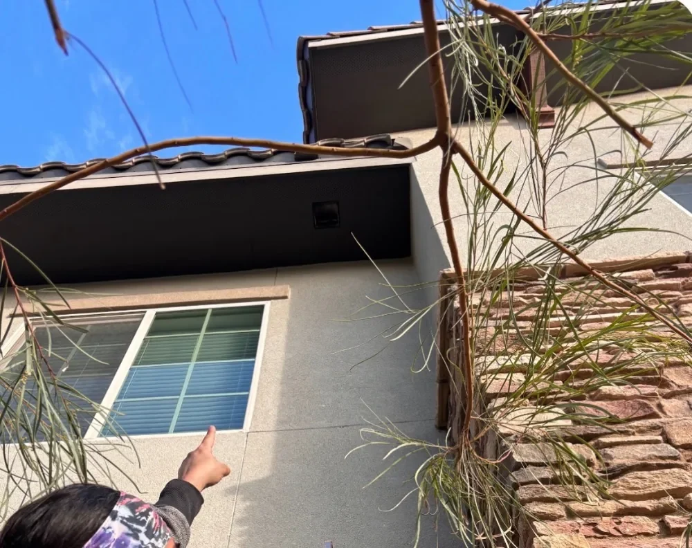 Pointing up at a dryer vent outlet high on a two-story stucco wall under the soffit